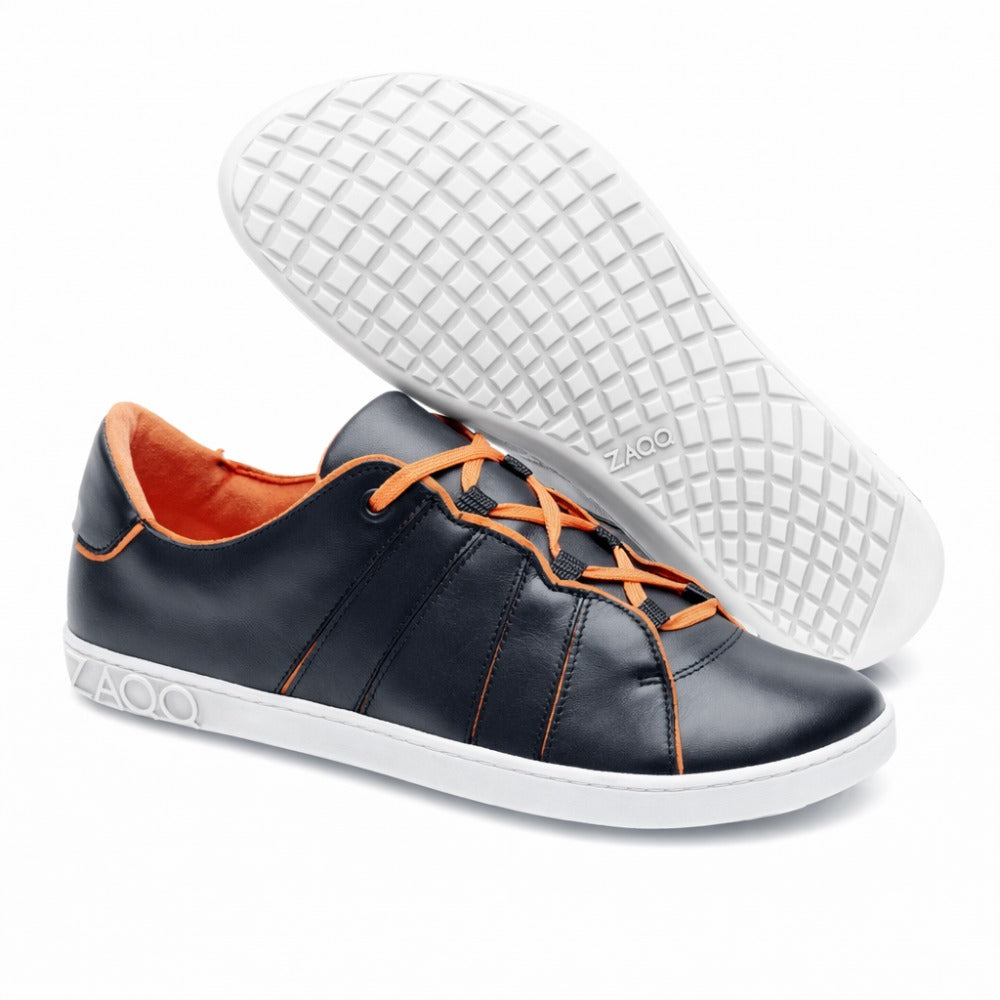 Ein Paar trendige ZAQQ QQQ Low Black Orange Sneaker mit schwarzem Obermaterial aus Leder, leuchtend orangefarbenen Schnürsenkeln und strahlend weißen Sohlen. Ein Sneaker steht aufrecht, während der andere seine gemusterte Sohle zeigt. Das Innere ist mit einem umweltfreundlichen, veganen orangefarbenen Futter versehen.